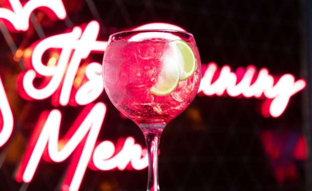 cutesy pink cocktail in a glass in front of a neon sign