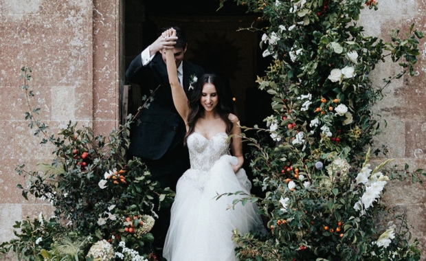 A newly-wed couple walking through a doorstep with a flower arrangement by Flowers By Passion